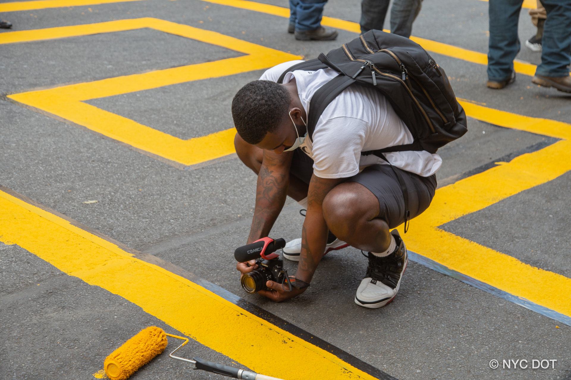André Davis crouching to film a scene with a handheld camera on a city street.