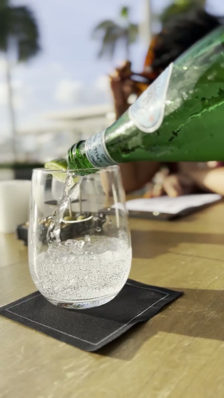 A sparkling drink being poured beside a sunlit resort pool.