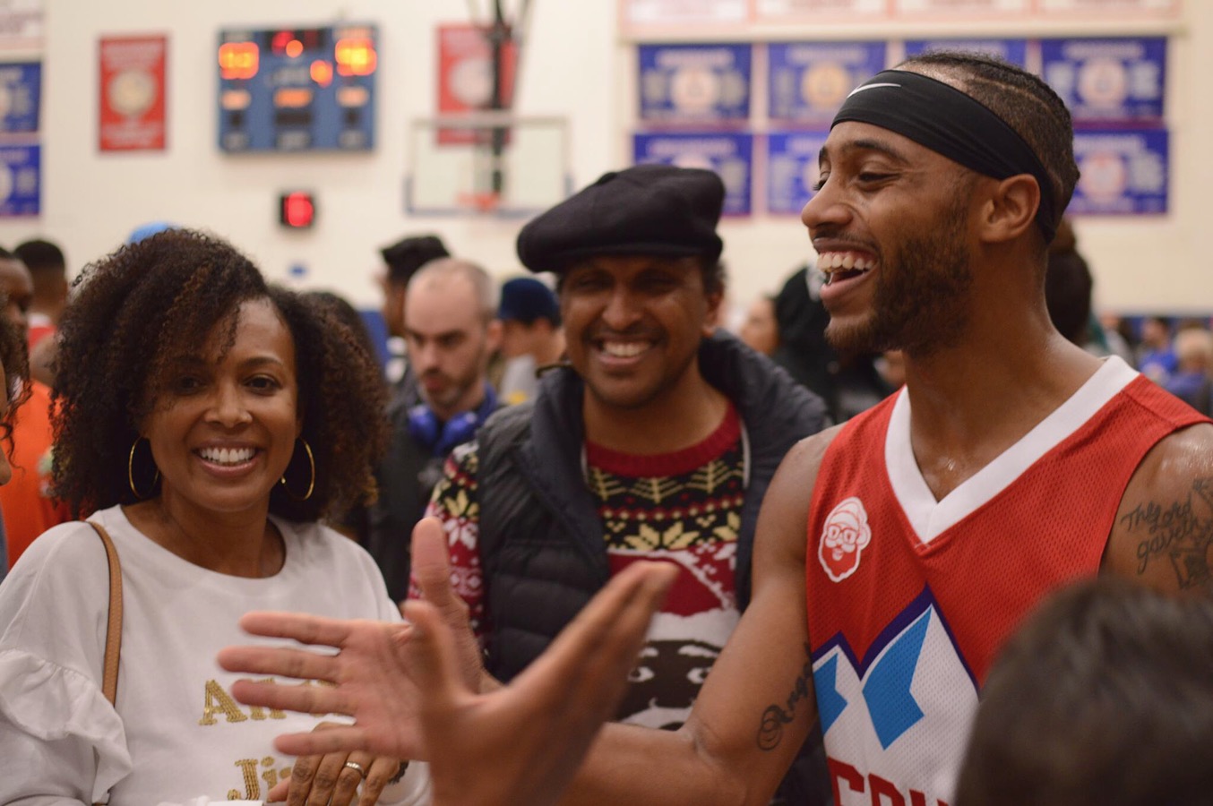 A player in a red basketball jersey greets attendees gathered on the court.